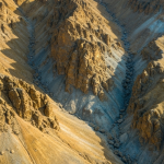 Geologischer Aufschluss in Nordkanada mit matten Goldtönen und kühlen blauen Schatten aus der Vogelperspektive
