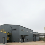 Industriegebäude einer Wolframverarbeitungsanlage unter grauem Himmel in gedeckten Grün- und Grautönen