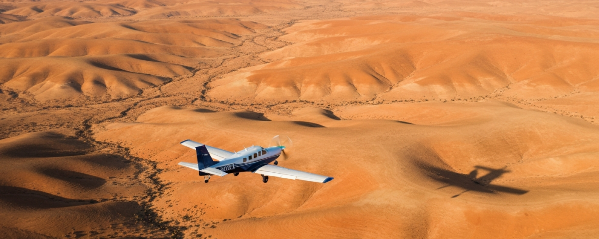 Kleines Vermessungsflugzeug im Tiefflug über einer weitläufigen Wüstenlandschaft bei Goldener Stunde