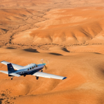 Kleines Vermessungsflugzeug im Tiefflug über einer weitläufigen Wüstenlandschaft bei Goldener Stunde