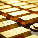 Goldbarren und Anlagemünzen auf dunklem Untergrund in warmem Licht