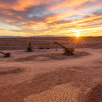 Wolframmine in Wüstenlandschaft bei Sonnenuntergang mit Bergbaumaschinen im Hintergrund