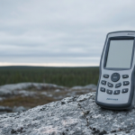 Geologe mit XRF-Analysegerät auf grauem Gesteinsaufschluss in borealer Landschaft