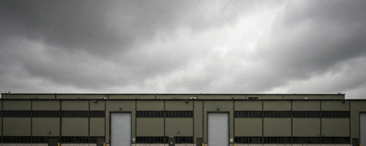 Rüstungsfabrik-Außengelände unter bedecktem Himmel in gedeckten Militärgrün- und Grautönen