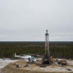 Luftaufnahme eines Bohrcamps im borealen Wald des Athabasca-Beckens mit Hubschrauber und Bohrgerät