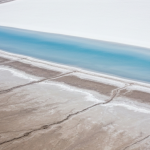 Luftaufnahme eines Salars mit weißer Salzkruste und himmelblauen Verdunstungsbecken bei Mittagslicht
