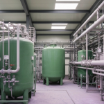 Seltene-Erden-Verarbeitungsanlage mit grünen Tanks und violetten Oxidrückständen in neutralem Industrielicht