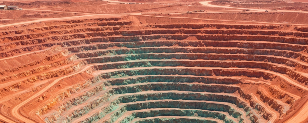 Luftaufnahme eines Kupfer-Tagebaus mit rötlich-orangefarbenen Felsterrassen und blaugrünen Oxidationszonen in Nordchile