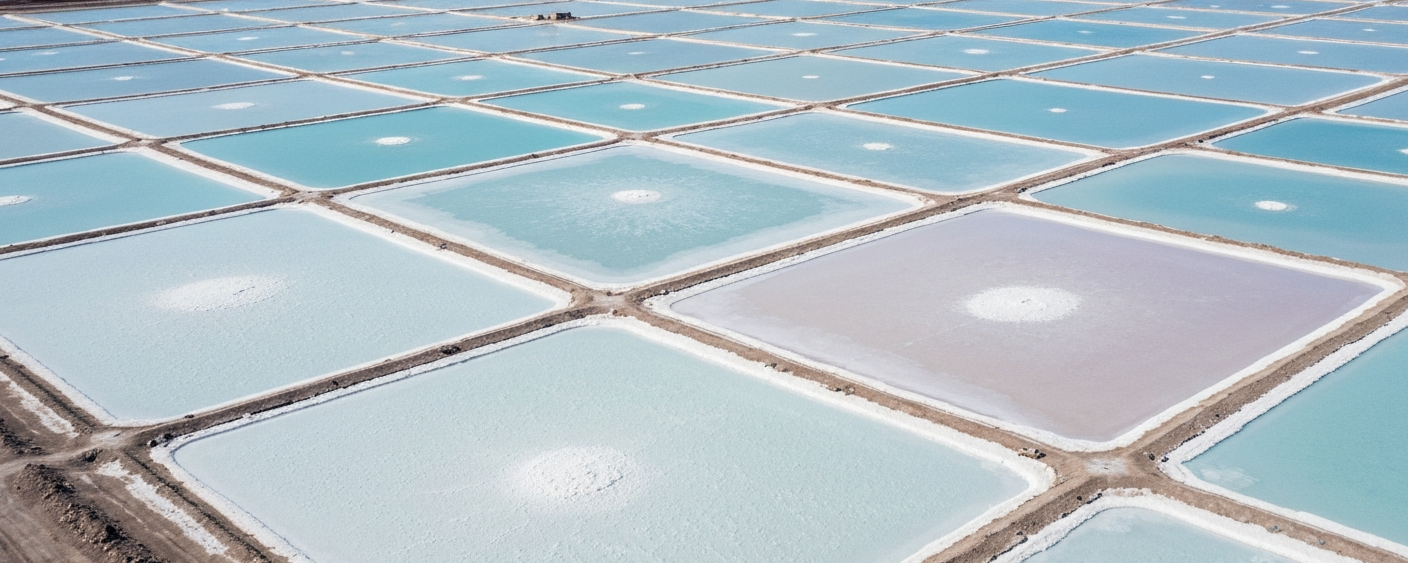 Aerial view of a lithium brine evaporation pond grid in a salar, with white salt crust and sky-blue ponds