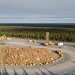 Luftaufnahme eines Bohrcamps in Nordkanada mit goldbraunen Gesteinsformationen und blauen Waldschatten