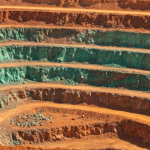 Luftaufnahme eines Kupfertagebaus mit rötlich-orangen Erzwänden und grünlichen Malachitspuren in Afrika