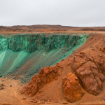Luftaufnahme eines Explorationsgeländes in den Anden mit rötlich-orangefarbenem Gestein und grünen Malachitspuren