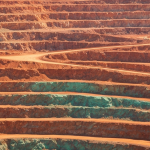 Luftaufnahme eines Kupfer-Tagebaus mit rötlich-orangen Erzterrassen und grünen Oxidationszonen