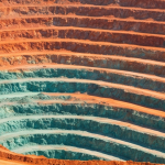 Luftaufnahme eines Kupfer-Tagebaus mit rotorangen Erzbänken und blaugrünen Oxidationszonen