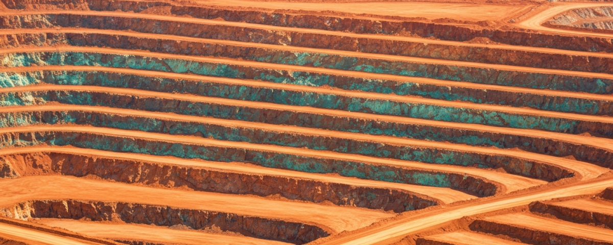 Luftaufnahme eines Kupfertagebaus mit rötlich-orangen Gesteinsformationen und blaugrünen Oxidationsspuren