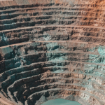 Luftaufnahme eines terrassierten Kupfertagebaus in den Anden mit rötlich-orangen Gesteinsschichten