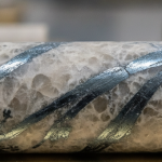 Bohrkern mit Quarzadern und dunklen Stibnit-Streifen auf einem geologischen Probentisch