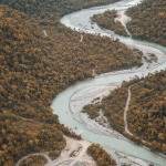 Weitläufige Luftaufnahme eines abgelegenen Flusstals in einer Frontier-Explorationsregion mit gedämpften Gold- und Bronz