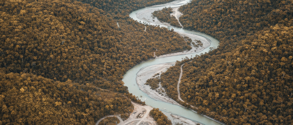 Weitläufige Luftaufnahme eines abgelegenen Flusstals in einer Frontier-Explorationsregion mit gedämpften Gold- und Bronz